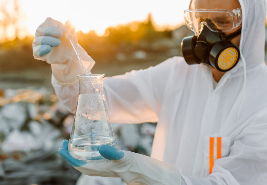 Ecologista em traje de proteção analisando amostra de produto químico tóxico — laudo de caracterização de resíduos industriais NBR 10005 10006