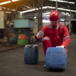 Operario industrial com EPI manuseando galoes de residuos quimicos perigosos Classe I para classificacao NBR 10004