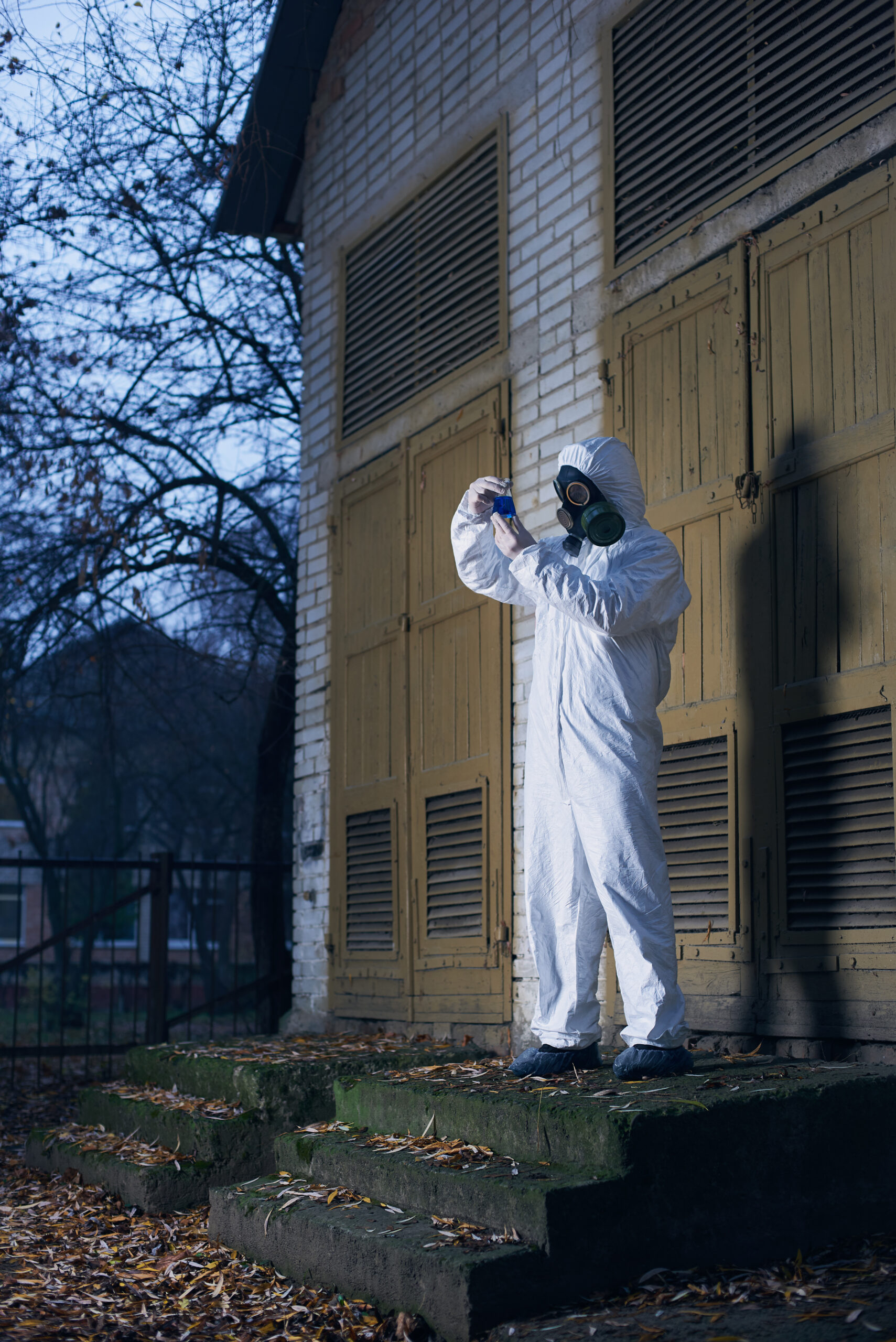 Cientista em macacão branco e máscara de gás realizando pesquisa ao ar livre — equipamento de proteção individual para remoção de amianto em edificações industriais