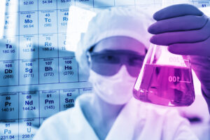 Cientista em laboratório químico industrial com máscara e tampa protetoras examinando tubo de ensaio — gestão de resíduos laboratoriais Classe I