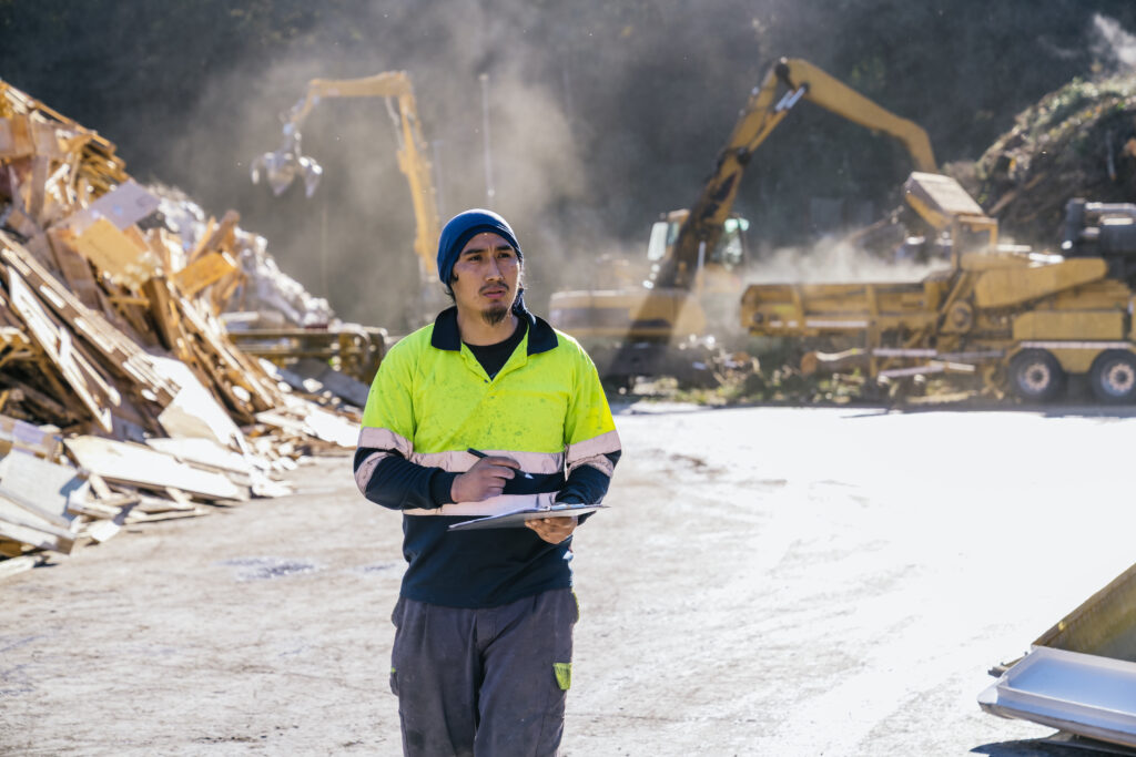 Trabalhador de gerenciamento de resíduos com prancheta avaliando operações de coleta industrial