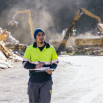 Trabalhador de gerenciamento de resíduos com prancheta avaliando operações de coleta industrial