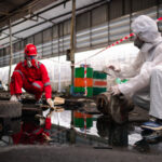 Trabalhadores em EPI completo realizando destinação de resíduos perigosos em instalação industrial